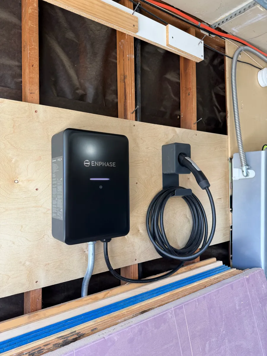 Enphase EV charger mounted on plywood in a garage under construction