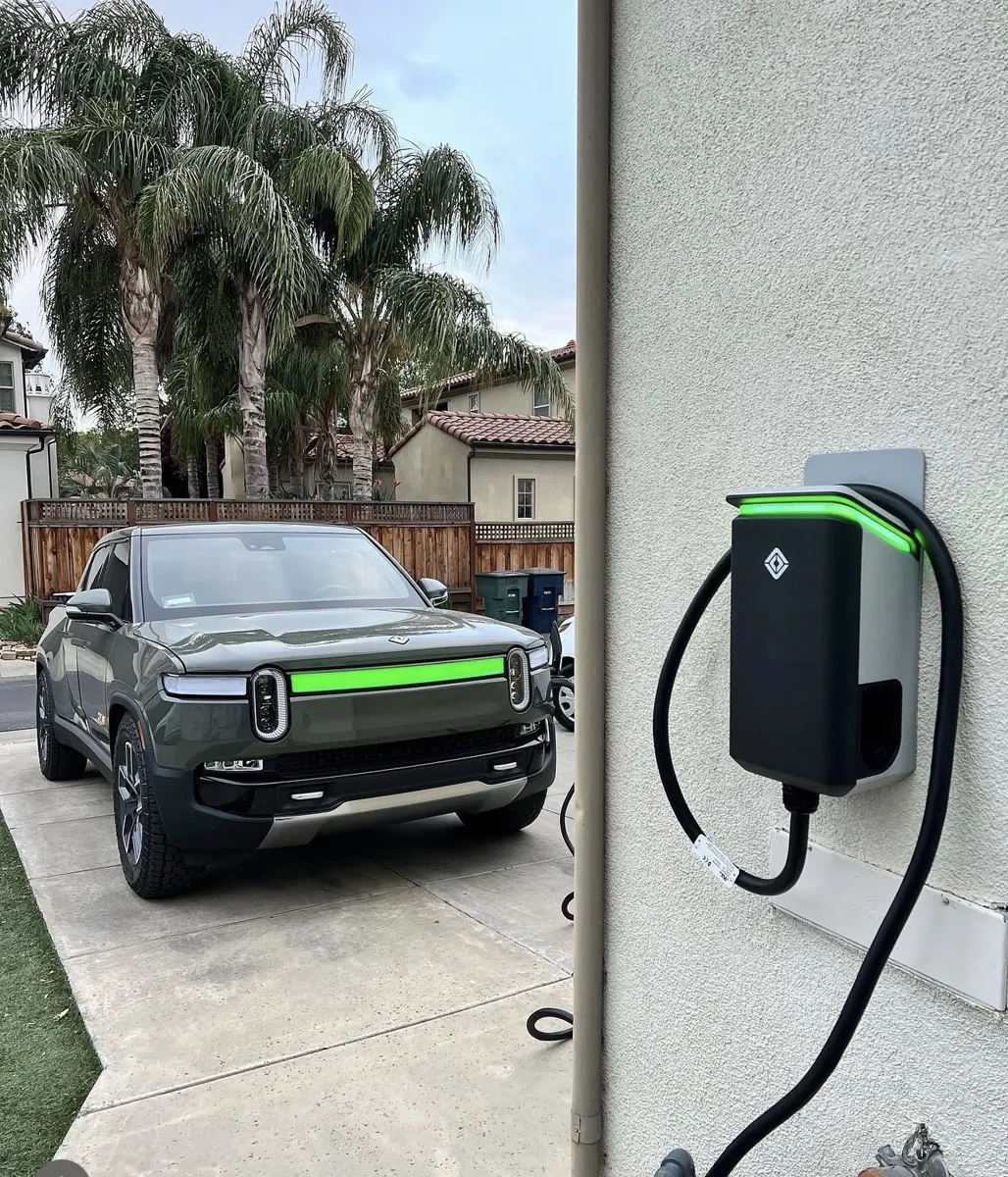 Rivian R1T truck in a driveway beside a newly installed Rivian Wall Charger glowing green