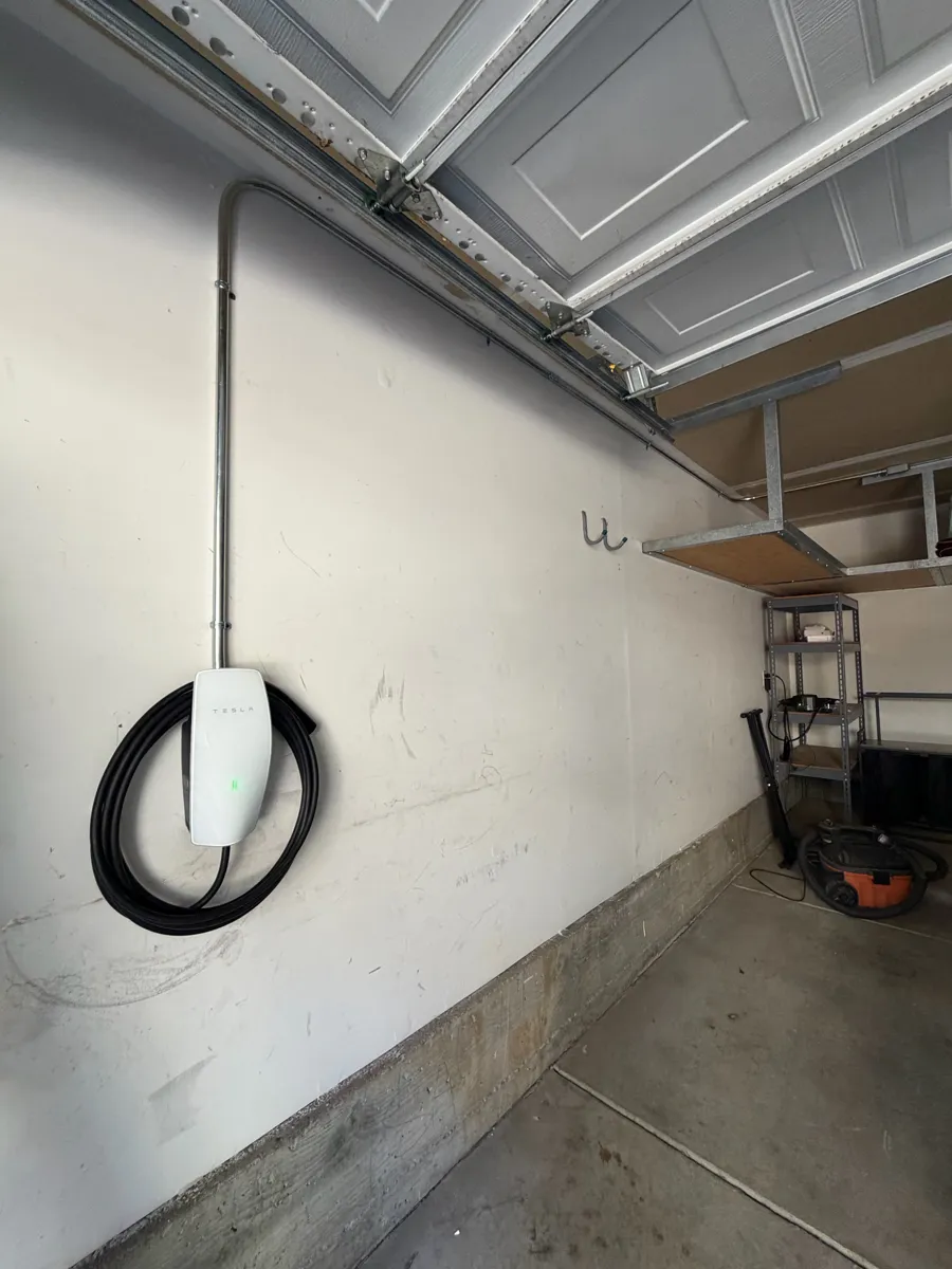 Tesla Wall Connector installed in a garage with conduit run along the ceiling